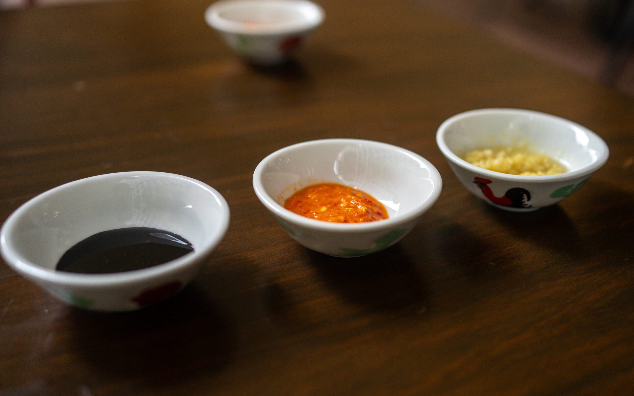 Assorted sauces for chicken rice at Nat's Chicks, including dark soy sauce, chili sauce, and ginger paste.