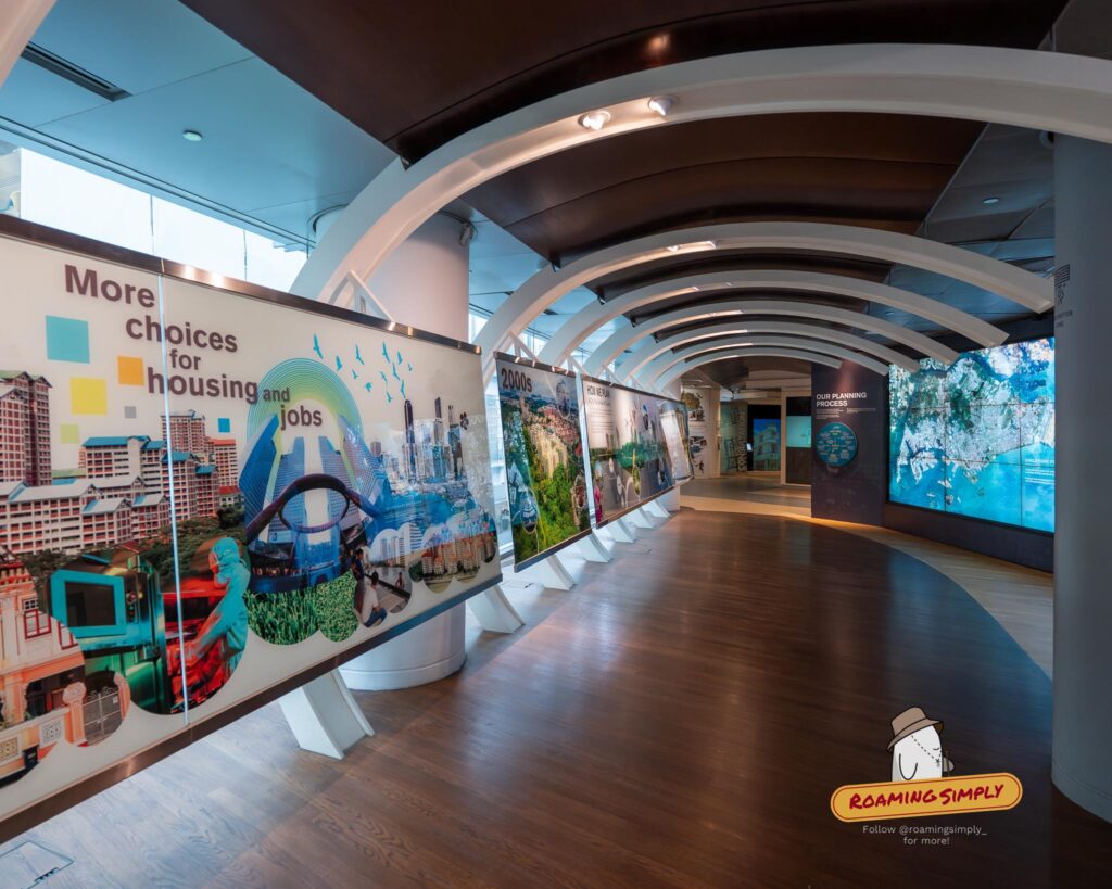 A curved wooden hallway in the Singapore City Gallery lined with illuminated exhibition panels that document the city's periods of progress and urban transformation.