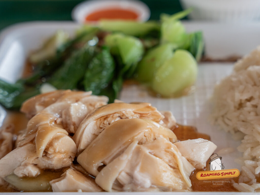 Close-up of Ah Tai Hainanese Chicken Rice set featuring tender steamed chicken slices with soy sauce, a side of blanched green vegetables, and a mound of fragrant rice.