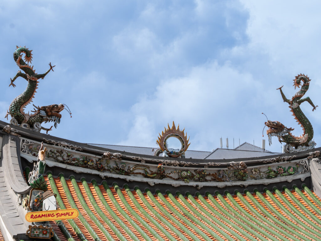 Close-up of the ornate roof ridge at Thian Hock Keng Temple featuring two dragon sculptures and green ceramic tiles against a blue sky.
