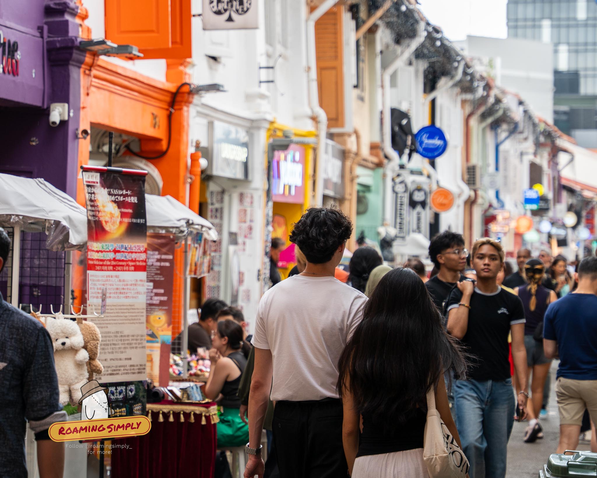 Crowds of people walking past colorful indie boutiques and street stalls on the narrow alleyway of Haji Lane in Singapore.