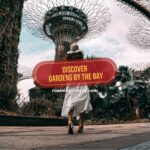 A woman in a white dress walking toward the iconic Supertree Grove at Gardens by the Bay in Singapore, featuring text that reads "Discover Gardens by the Bay."