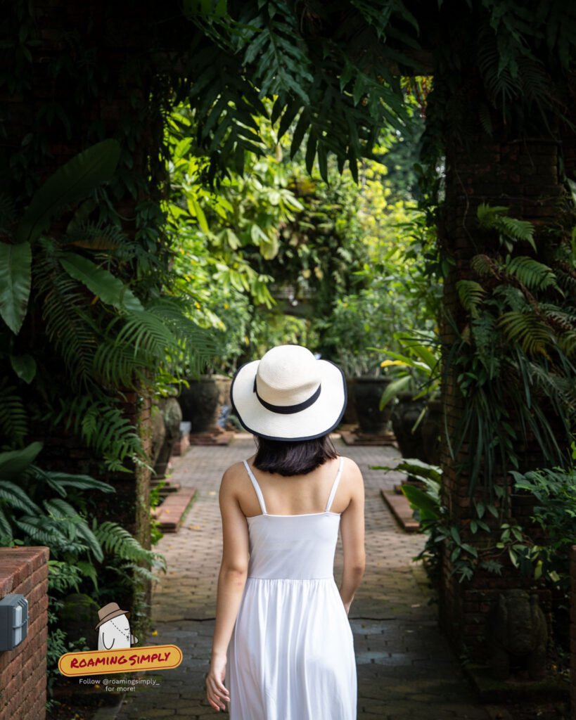 Woman in a straw hat walking a fern-lined garden path at Fort Canning Park, Singapore