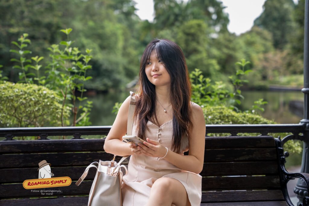 Yi Yun sitting on a wooden bench overlooking Swan Lake at Singapore Botanic Gardens.