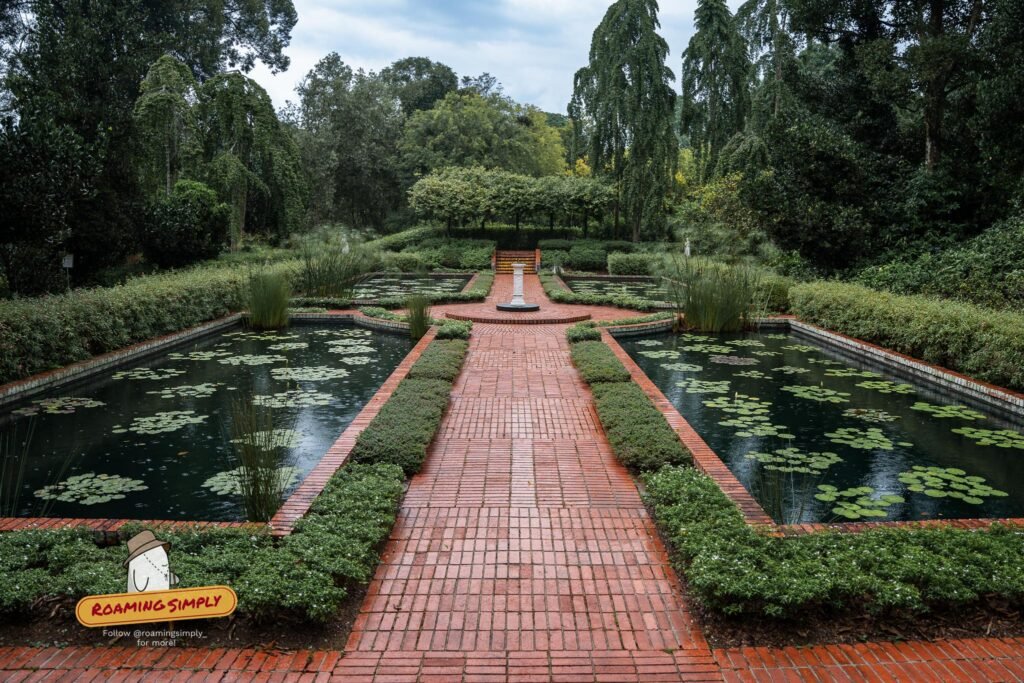 The Sundial Garden at Singapore Botanic Gardens, with a red brick path running between two symmetrical lily pools towards a white sundial at the far end.