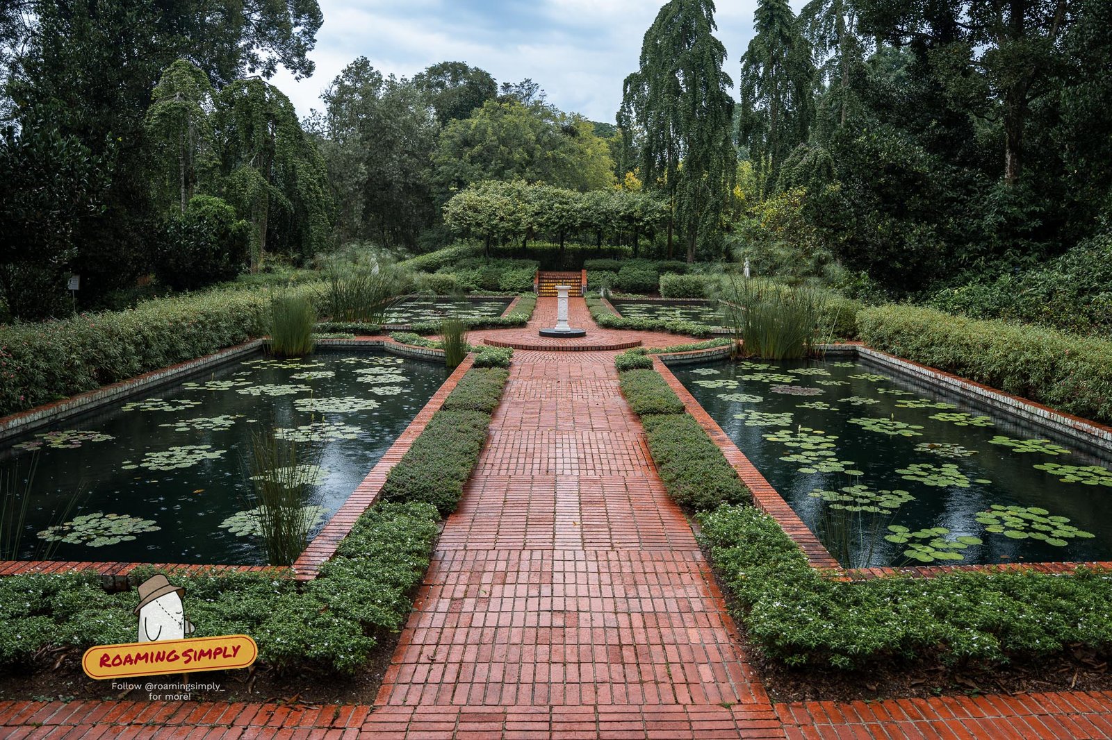 The Sundial Garden at Singapore Botanic Gardens, with a red brick path running between two symmetrical lily pools towards a white sundial at the far end.