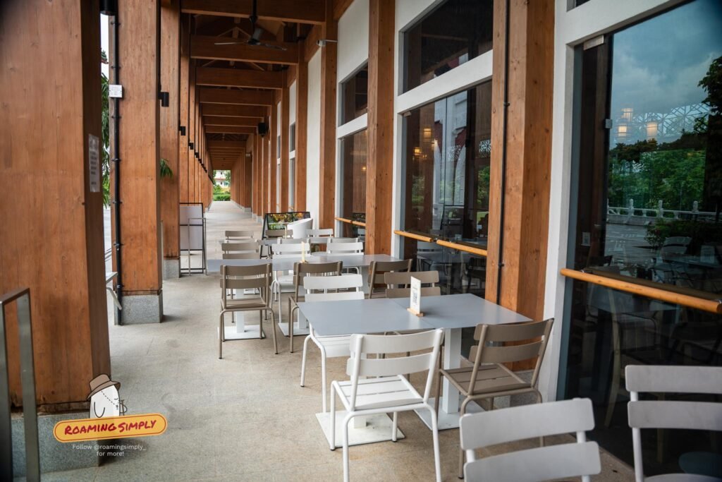 Grey metal tables and chairs along a covered timber colonnade with ceiling fans, facing the garden