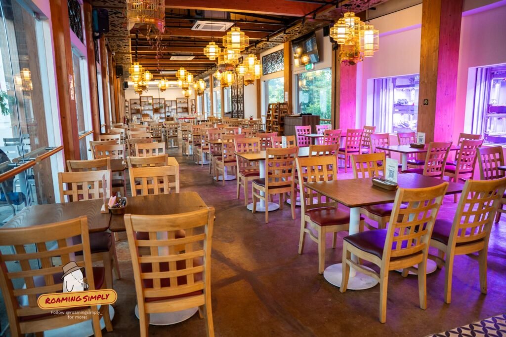 A long indoor dining room with timber tables, lattice-backed chairs and rows of birdcage pendant lanterns