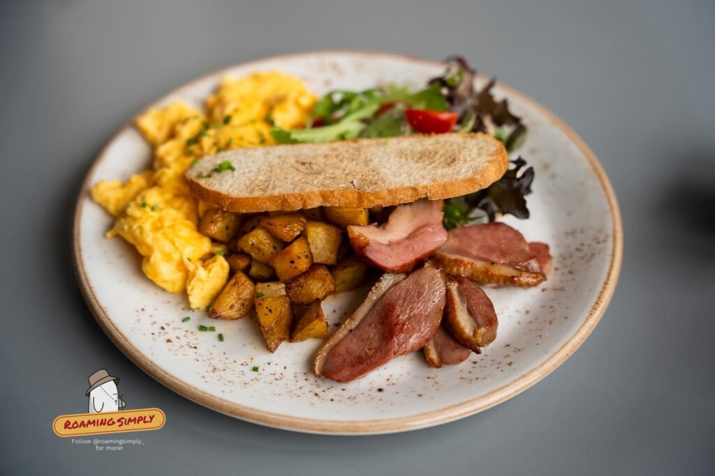 A plate of scrambled eggs, sliced smoked duck, roasted potato cubes, toasted sourdough and salad