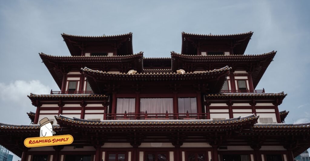 Red and white upper storeys of the Buddha Tooth Relic Temple, with tiered tiled roofs against a grey sky