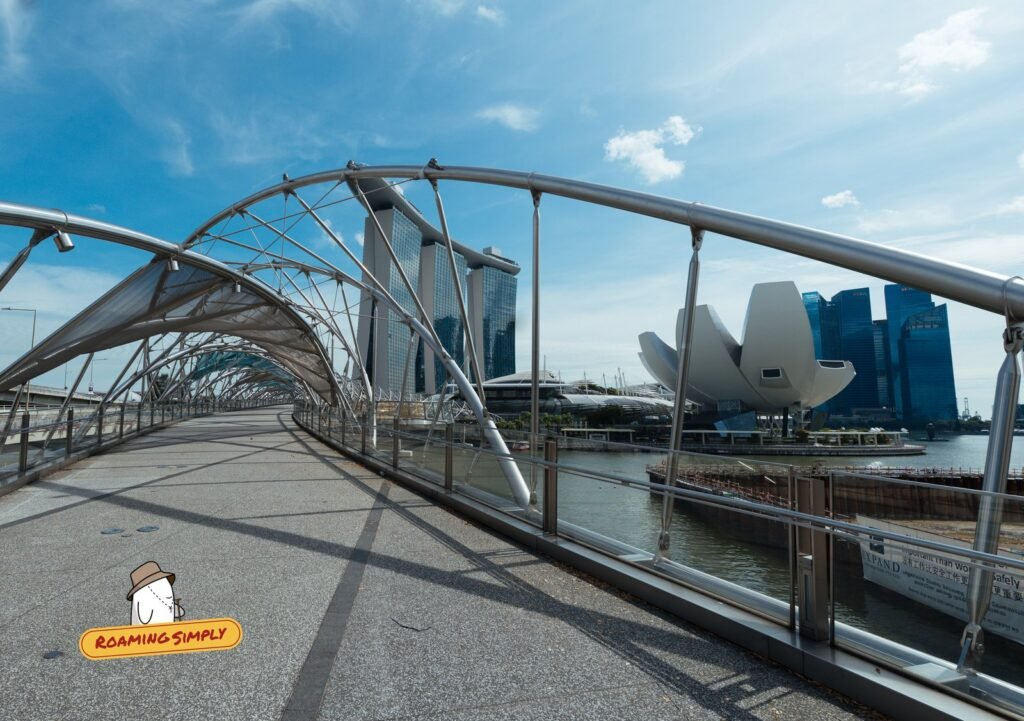 Walkway of the Helix Bridge under its steel spiral frame, with Marina Bay Sands and the ArtScience Museum beyond