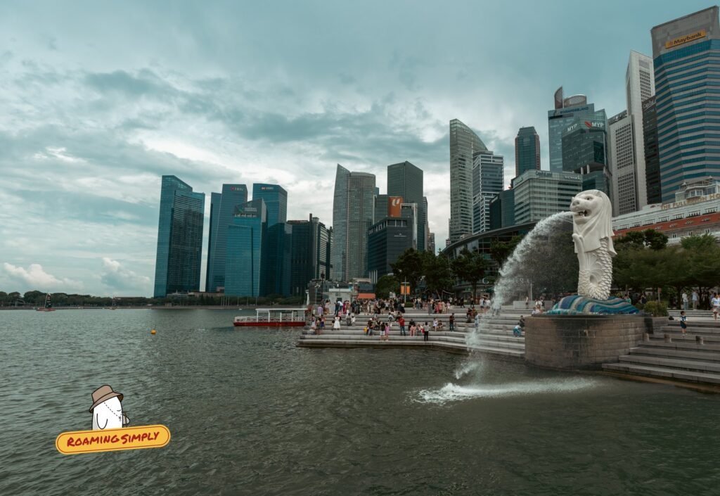 Merlion statue spouting water into Marina Bay, with crowds on the steps and office towers behind