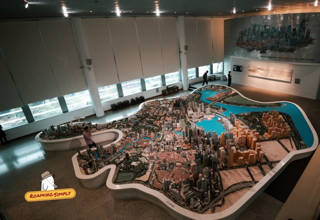 Large scale model of central Singapore seen from above in a gallery hall, with visitors standing beside it